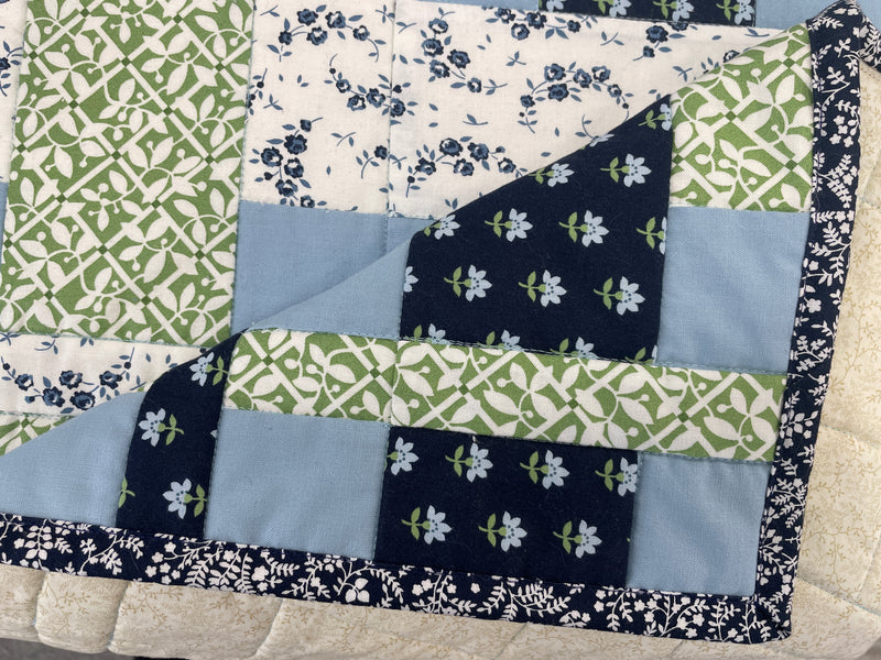 A Close Up showing the corner of a quilt bound with a navy binding. It shows a mitered corner. 