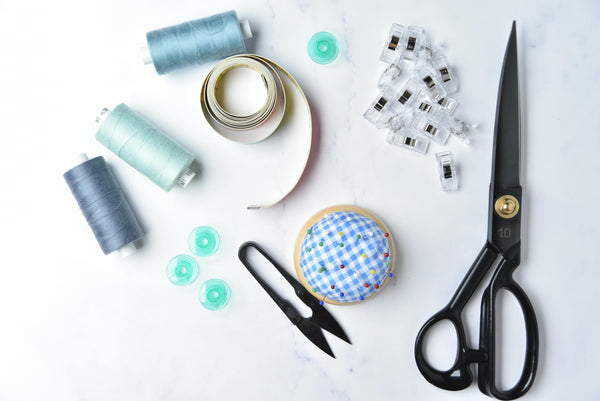 A stock image of sewing supplies including bobbins, thread trimmers, wonder clips, and scissors