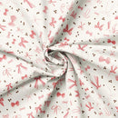 Fabric patterned with pink bows and espresso beans on a cream background. It is folded to show the weight of the fabric. 