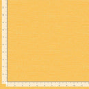 A close-up of a fabric or material swatch in warm mustard yellow with a fine dotted texture, shown with ruler markings along the left and bottom edges for scale.