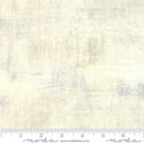 A swatch of tonal cream fabric featuring a blend of light gray and greige tones. There is a Moda branded ruler at the bottom for scale. 