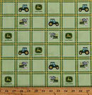 A close-up of a fabric pattern featuring a green and yellow plaid background with repeating John Deere tractor and logo motifs, plus a wooden ruler along the bottom edge showing measurements.