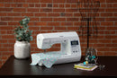 An example of a Brother PS500 sewing machine on a desk with a brick wall behind it. 