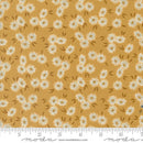 Fabric patterned with small clusters of white flowers on a yellow background with a moda branded ruler for scale