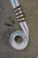 A coiled roll of white zipper tape with rainbow metallic teeth and rainbow metallic zipper pulls