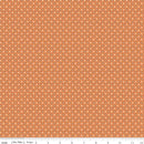 Fabric featuring a small geometric pattern on an orange background with a riley blake branded ruler for scale. 