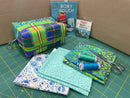 An image of a sample completed boxy pouch, alongside the pattern, hardware, colorful fat quarters, thread, and sewing scissors