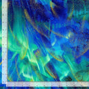 Fabric swatch featuring a multicolored blue and teal aurora on a dark blue night sky with gold metallic accents. There is a ruler along the left and bottom edge for scale. 